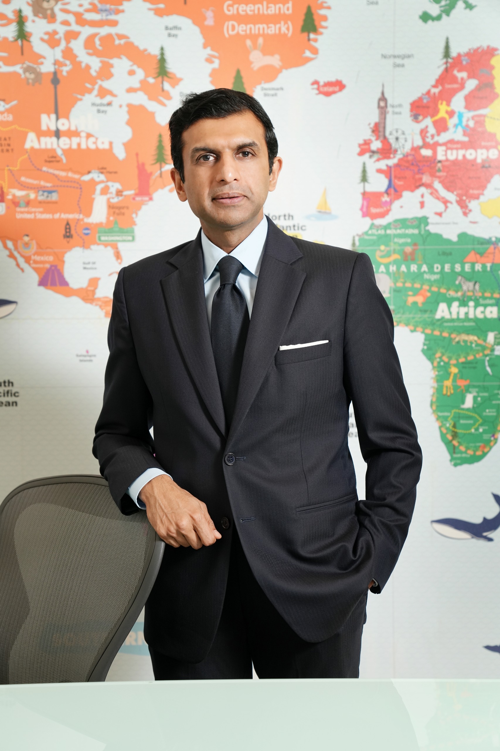 Man in a dark suit and tie standing in front of a colorful world map
